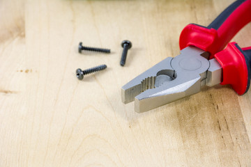 Pincers with screws on wooden background