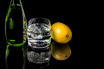 Bottle and glass water with lemon on black background
