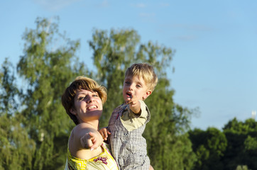 Portrait of happy mom kissing and shake son on green summer garden. Cute  mother embracing baby boy looking at camera