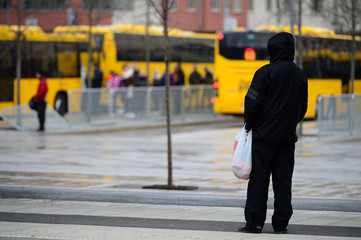 Man in raincoat in rain waiting for bus