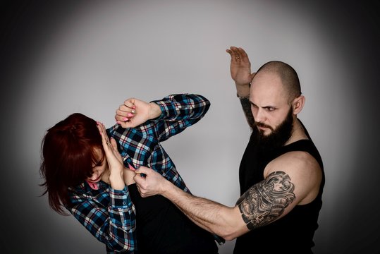 Muscular bearded man beating his redhead wife.