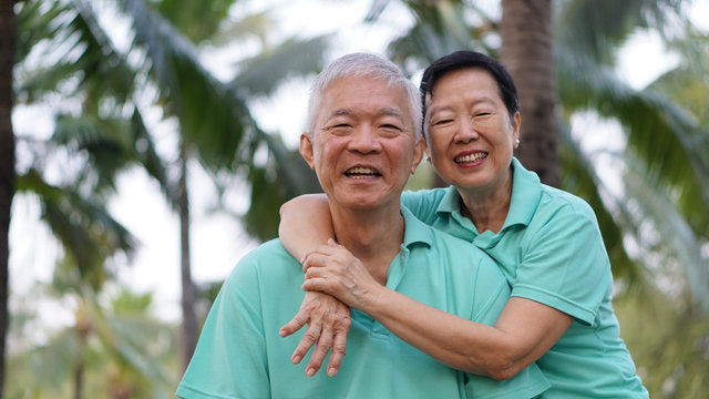 Asian senior couple relaxing in the park laughing in sunshine