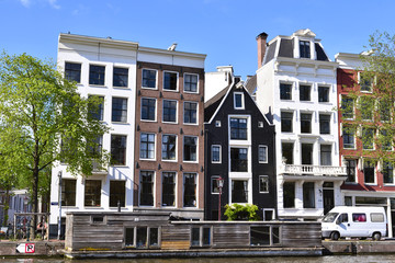 Amstel river, canal of Amsterdam with old houses and wooden houseboat. Fresh green trees and blue sky. Amsterdam in summer.