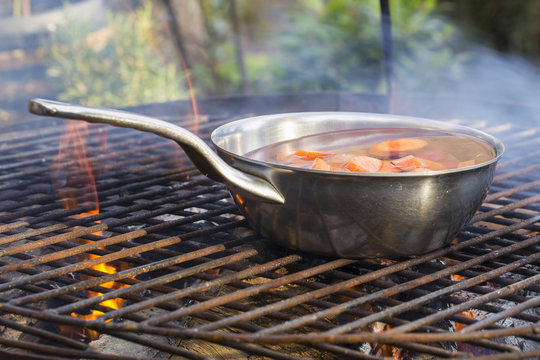 A small pan on a fire with blanched carrots. 