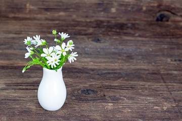 Bouquet of white wildflowers in porcelain vase, wooden background