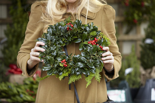 A woman carrying a decorated wreath of holly and evergreen leaves. 