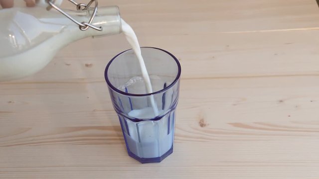 Fresh milk is poured from a glass bottle into the glass tumbler.