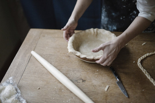 A woman working smoothing the edge of a pastry case lining a pie dish. 