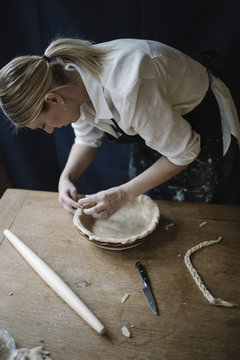 A woman working smoothing the edge of a pastry case lining a pie dish. 