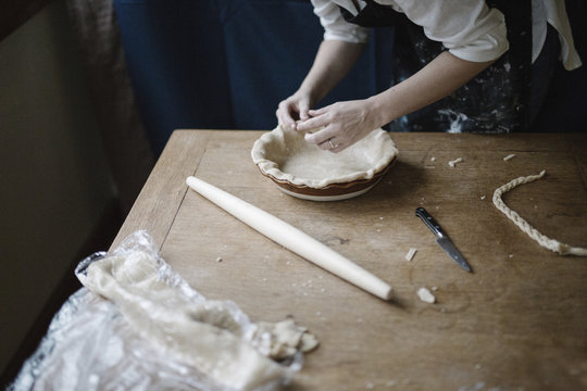 A woman working smoothing the edge of a pastry case lining a pie dish. 