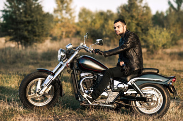 Fototapeta na wymiar young brutal man in a black jacket and glasses sits near a motorcycle.