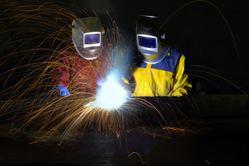 Industrial workers cutting and welding metal with many sharp sparks,