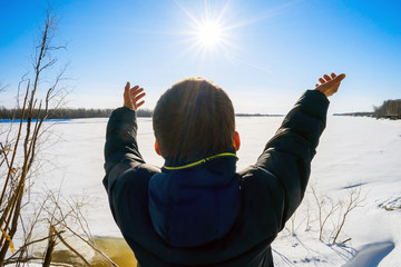 The boy stands on  shore  frozen river and pulled by hand to sun.