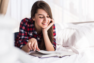 leisure reading woman is comfortable lying on her bed with a book, smiling and happy and dreaming