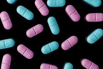 Scattered pink and blue pills on black background directly from above