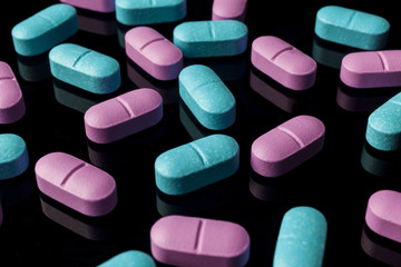 Scattered pink and blue pills on black background from side