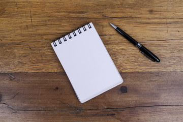 White sheets notebook with spiral in the center of the wooden dark brown table with black pen on side from above