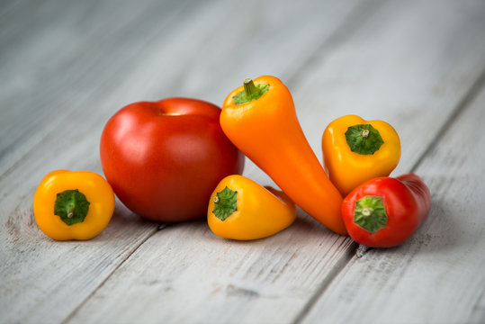 Red tomato and mini colored sweet peppers on a wooden background