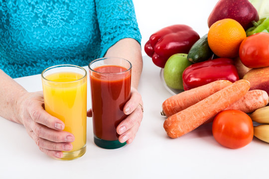 Woman puts two glasses with orange and tomato juice on the table with vegetables and fruits