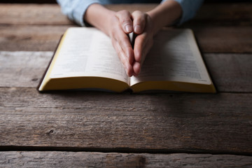 Naklejka premium Woman hands praying with a bible in a dark over wooden table