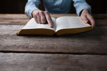 Woman hands praying with a bible in a dark over wooden table