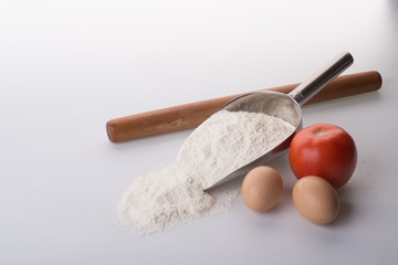Flour in bowl with eggs and rolling pin over white background