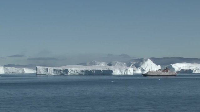 View of the icebergs of Disko Bay, Ilulissat, Greenland with a small cruise ship in the background
