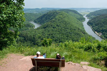 Couple resting on a bench with view from Cloef to Saarschleife, Saar river, Germany