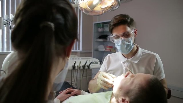 young dentist and his assistant treat teeth middle-aged man