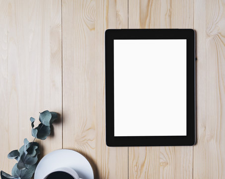 Tablet with a clean blank screen monitor with a branch of eucalyptus and a cup of coffee on a wooden background with natural wood planks top view horizontal, display and space for publicity text
