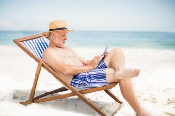 Senior man using tablet at the beach - Powered by Adobe