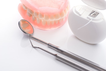 Teeth model with dental floss and mouth mirror on white background