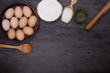 Wooden background with baking ingredients (eggs, flour and rolling pin) over rustic texture. Top view. Space for text. Food or cooking concept.