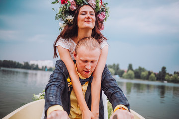 Fototapeta na wymiar bride and groom sitting in an orange row boat floating out of the tree covering and in to the lake. Bride with wreath of flowers