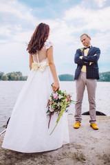 Stylish young bride and groom running on the pier near the boat against the backdrop of lakes.