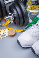 Dumbbells with measuring tape, trainers, pills and bottle of chilling water