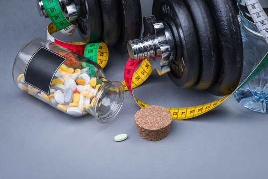 Heavy classical dumbbells with measuring tape and pills on grey