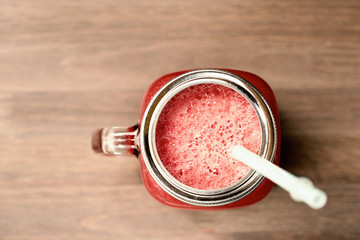 A watermelon smoothie in a mason jar with tube on wooden background. Sepia toning