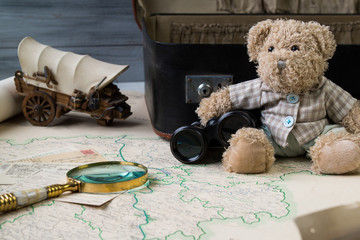 Travel concept, teddy bear with old binoculars and suitcase on the antique map with magnify glass