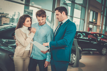 Salesman talking to a young couple at the dealership showroom.