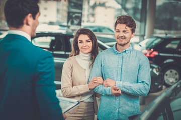 Obraz premium Salesman talking to a young couple at the dealership showroom.