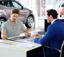 Handsome young man reading a booklet at the dealership showroom.