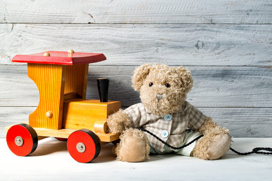 Teddy bear and the toy wooden train, wooden background