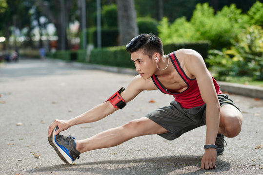 Asian young jogger stretching his legs outdoors