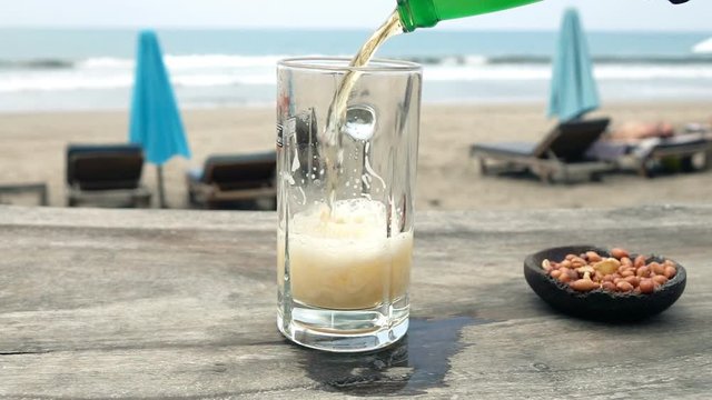 Pouring beer in glass on wooden table in beach bar, super slow motion 240fps
