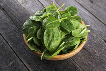 Spinach leaves in bowl on dark wooden background