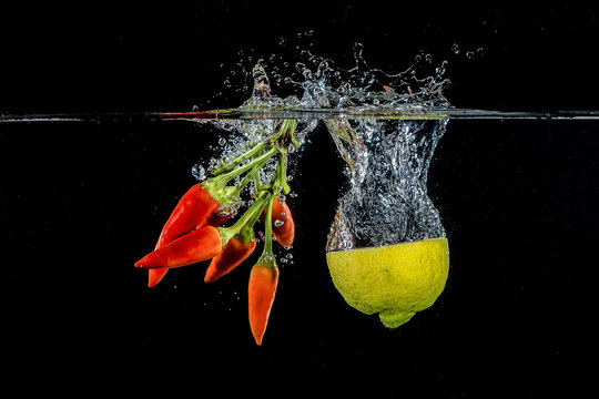Mezzo limone e mazzo di peperoncini rossi tuffati in acqua su sfondo nero