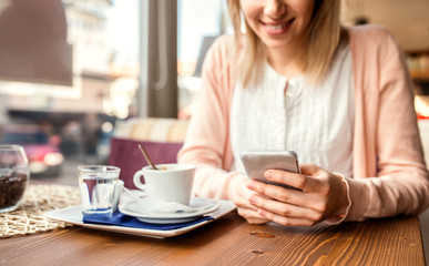 Unrecognizable woman with smartphone in cafe drinking coffee