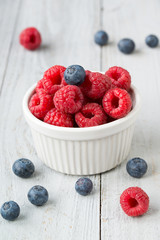 Bowl with raspberries and blueberries on wooden background