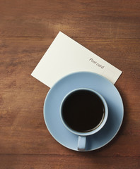 Cup of black coffee with postcard on wooden texture